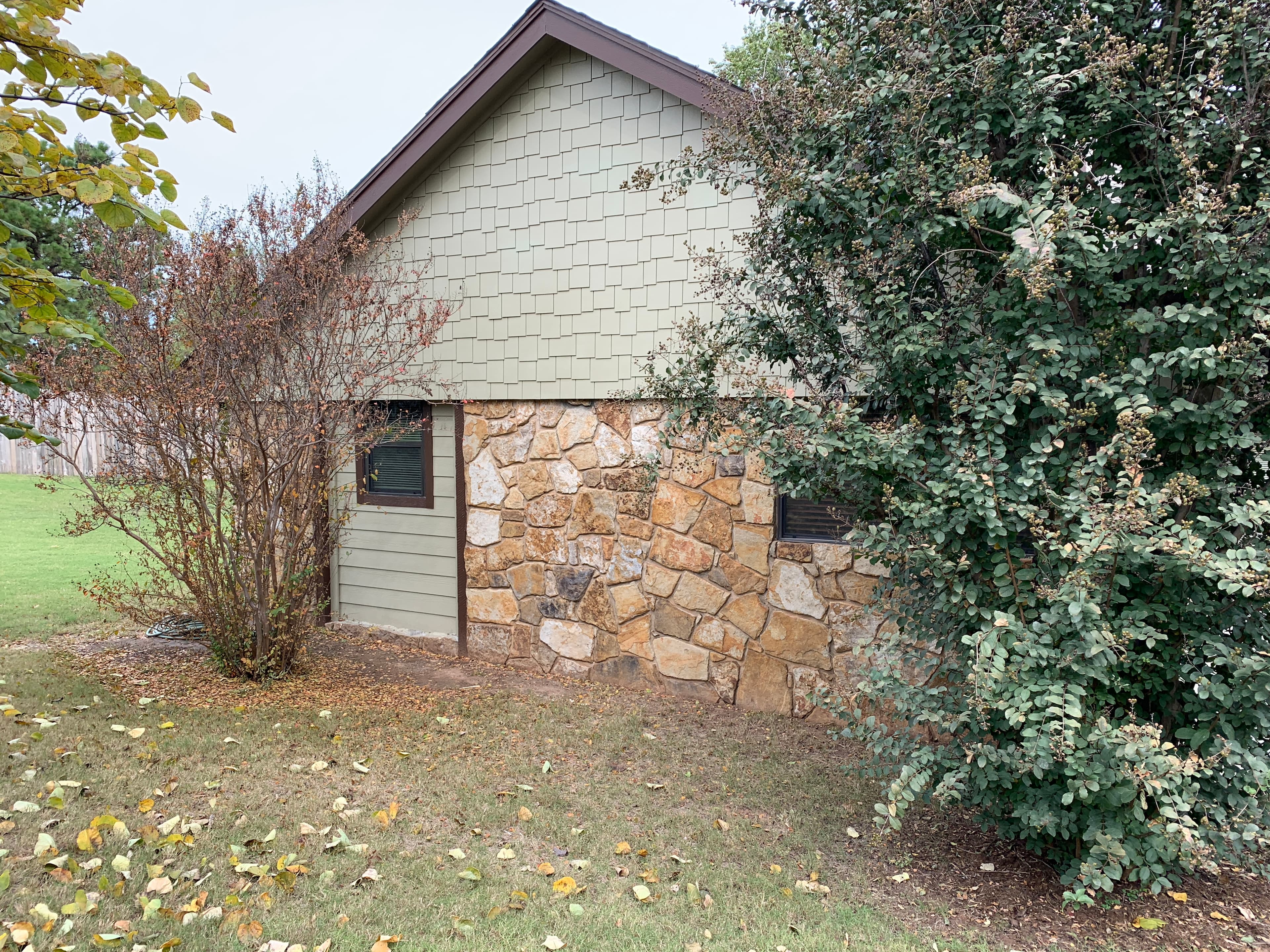 Side gable elevation of an Edmond home displaying natural stone veneer siding, green accent shakes, and clean roof edges.