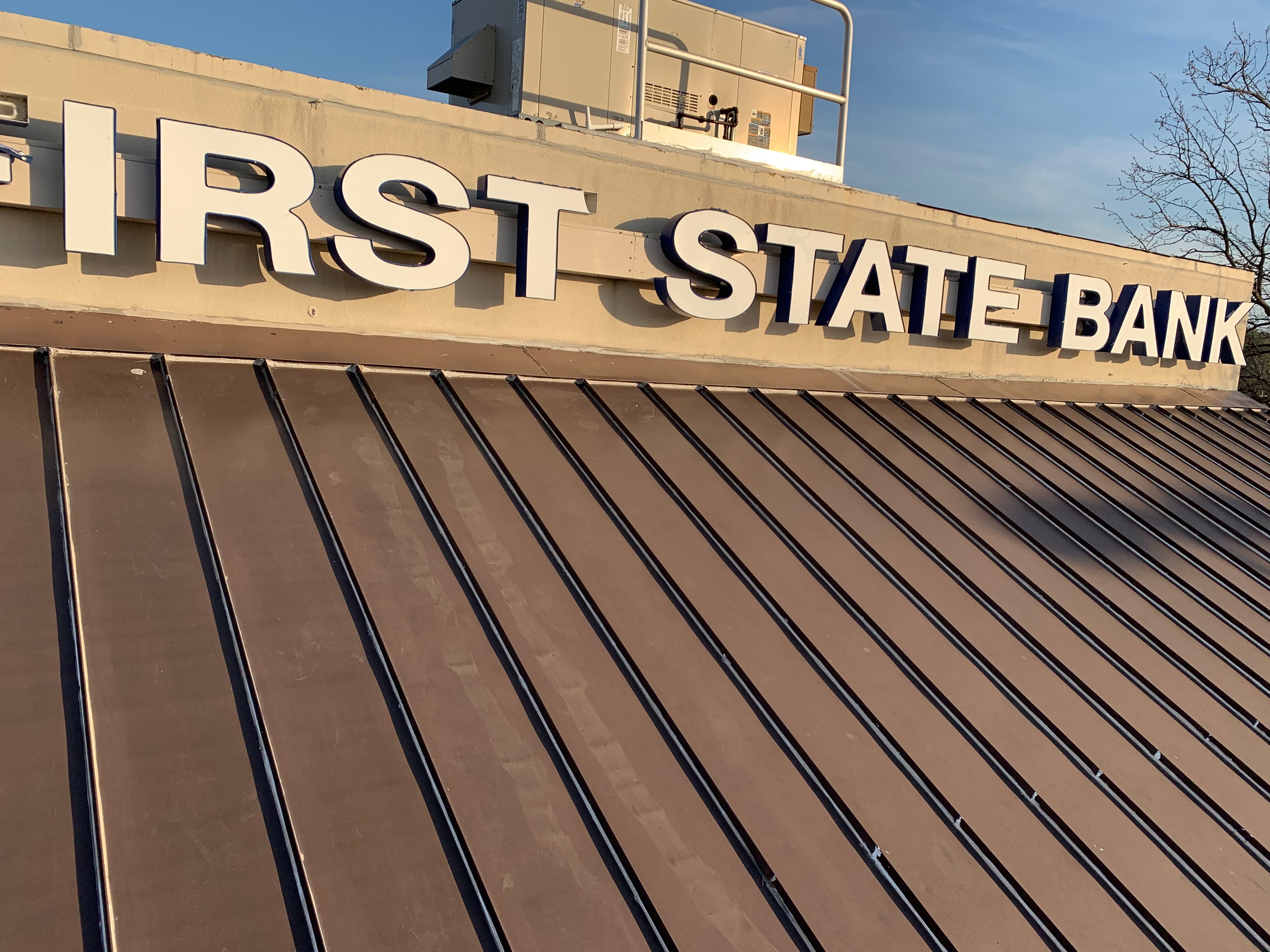 Close-up of bronze standing seam metal roof panels installed directly underneath First State Bank exterior building signage.