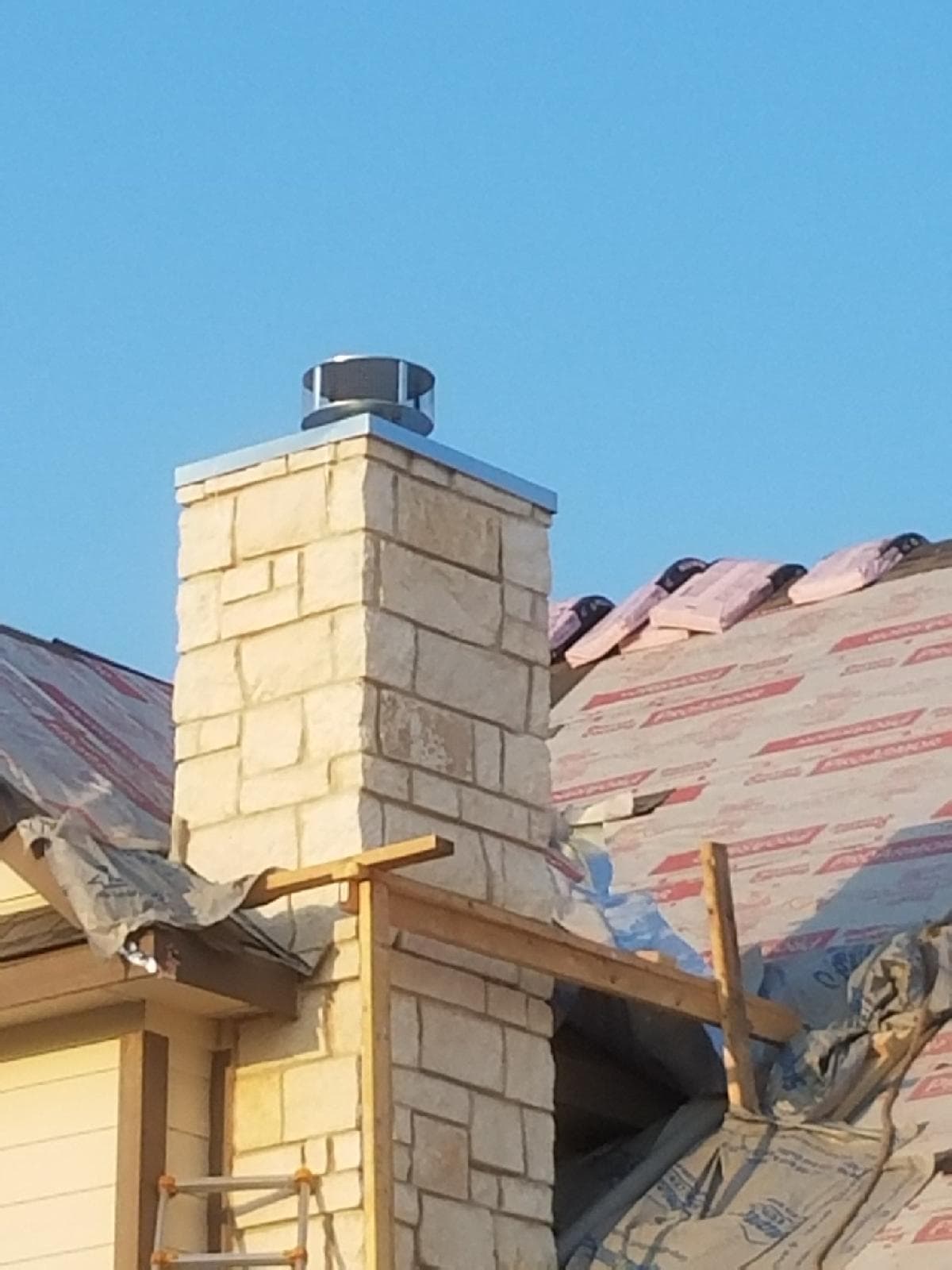 Stone chimney featuring a stainless steel cap surrounded by synthetic roof underlayment during construction.