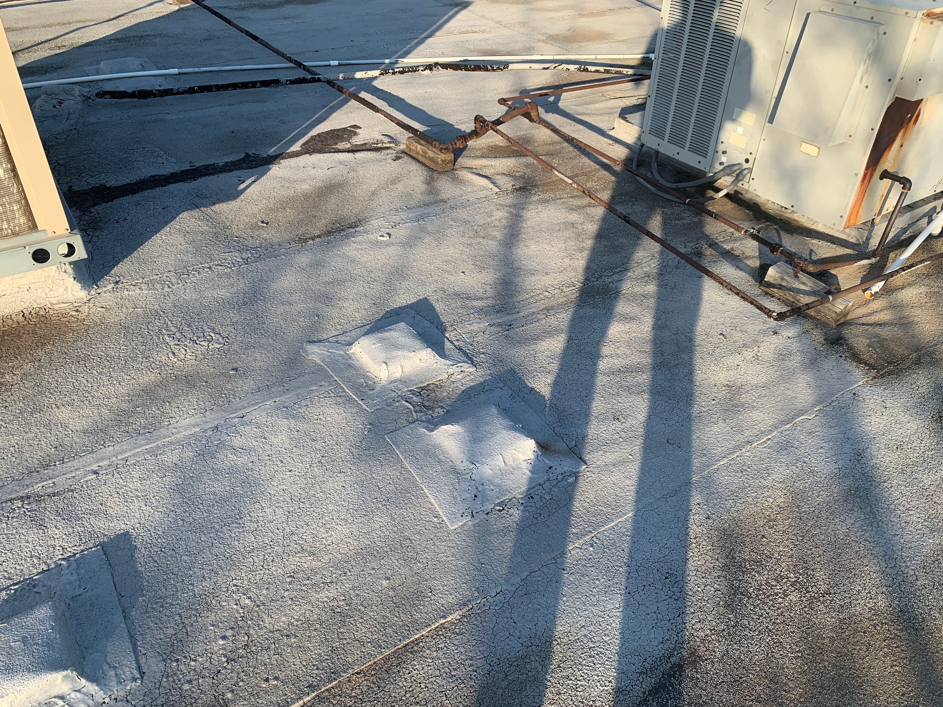 Top view of a white elastomeric coated commercial flat roof featuring gas piping and rooftop HVAC unit curbs.