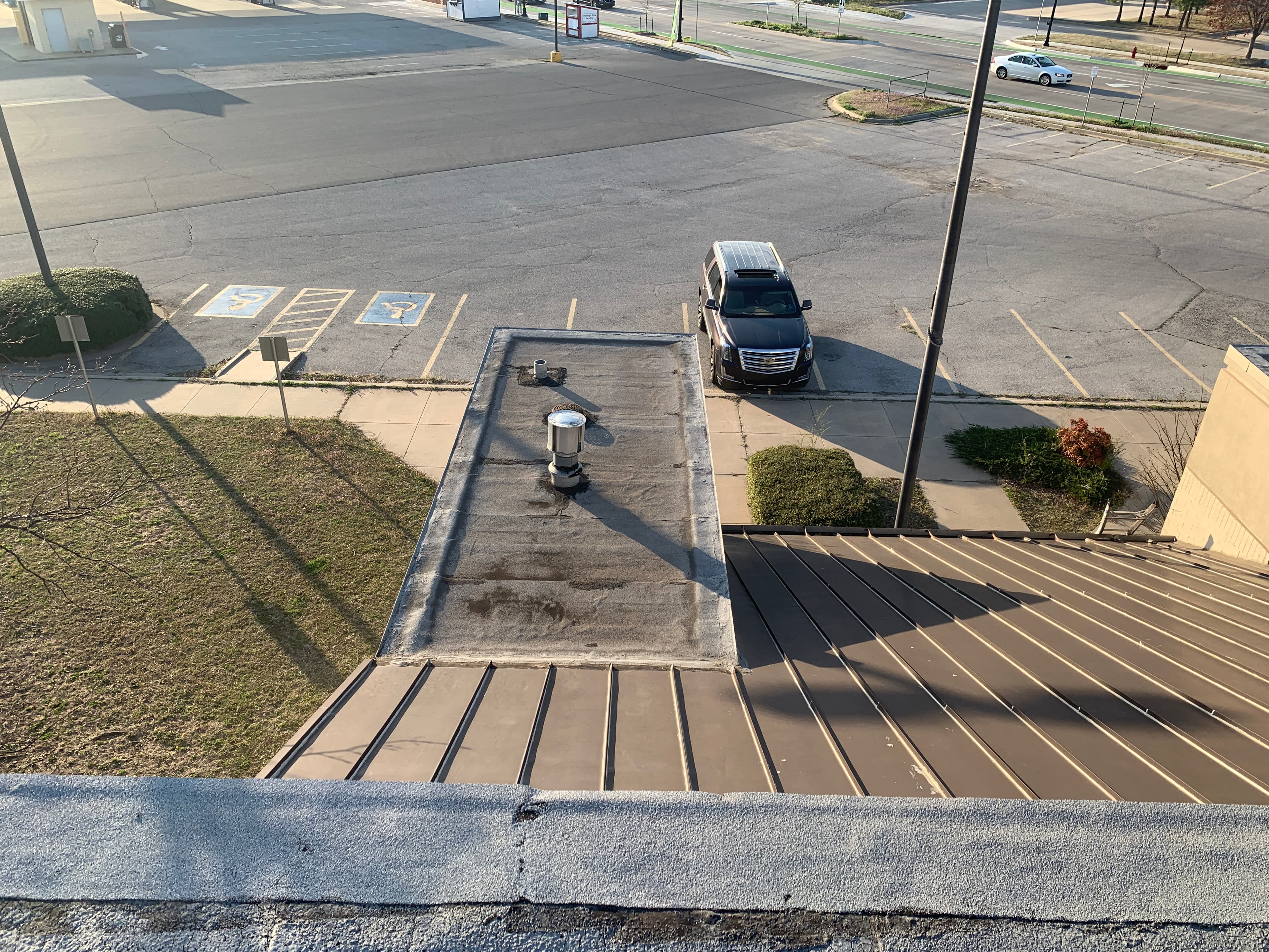 Elevated rooftop view looking down at a standing seam metal awning transitioning into a low-slope flat roof section.