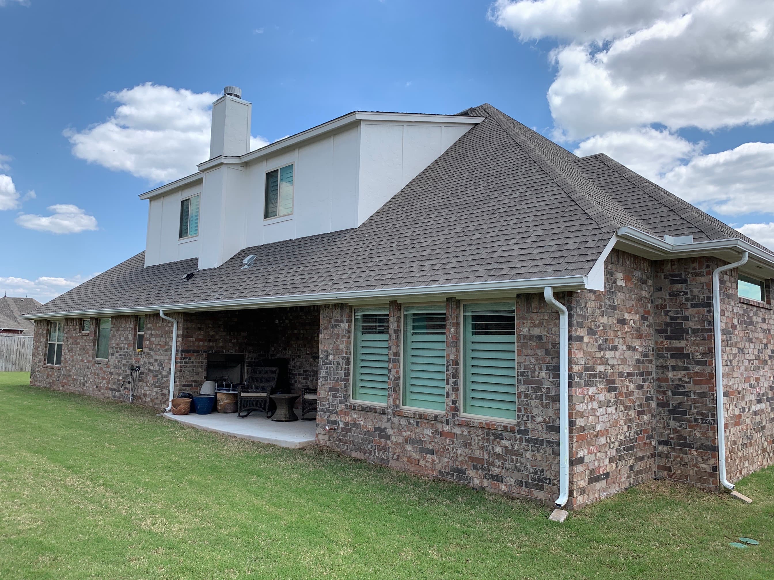 Rear yard view of a two-story brick residence in Oklahoma City showing new steep-slope shingle roofing over a covered patio.