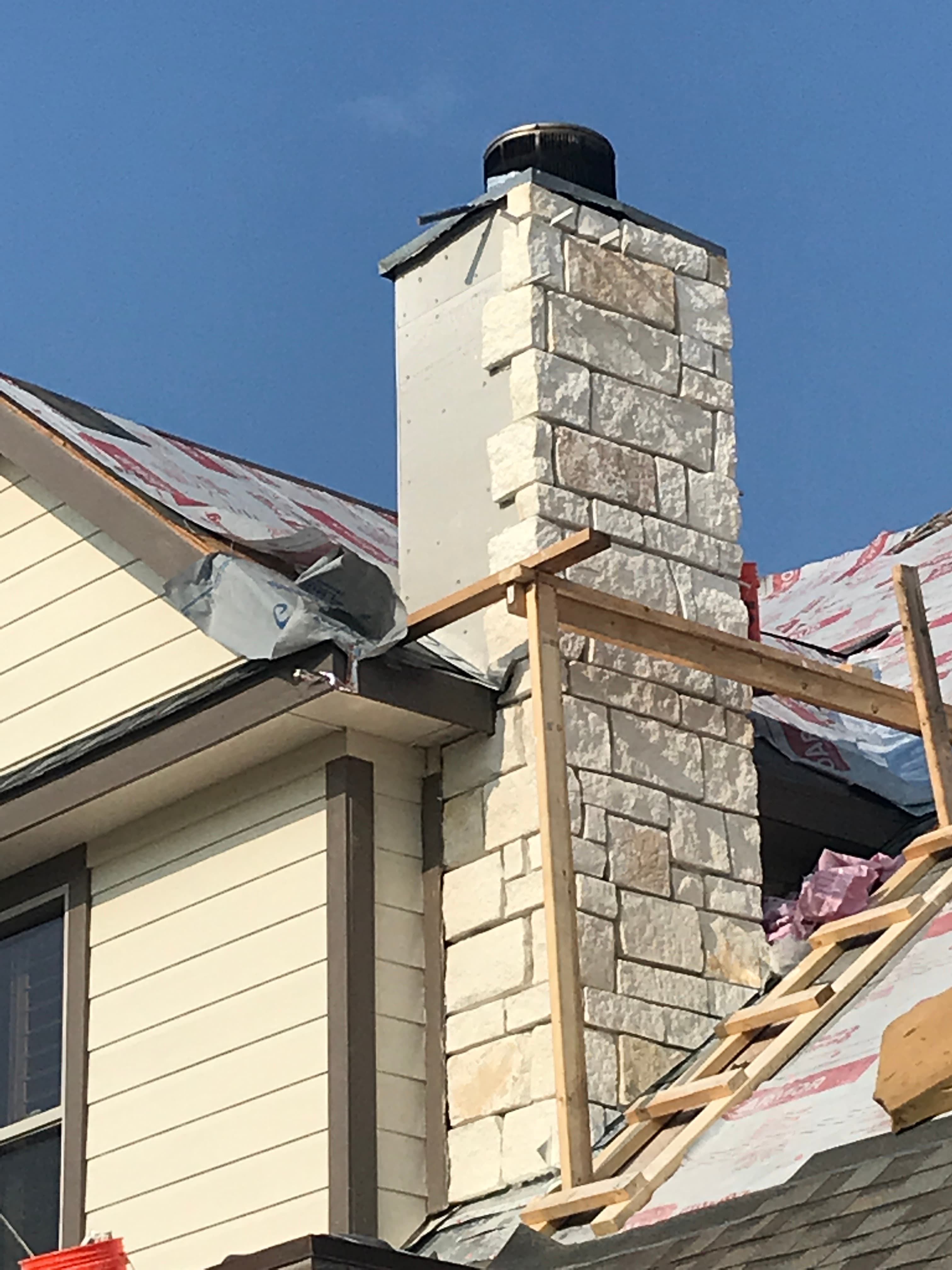 Close-up of custom wooden scaffolding built around a stone chimney during a residential roof tear-off.