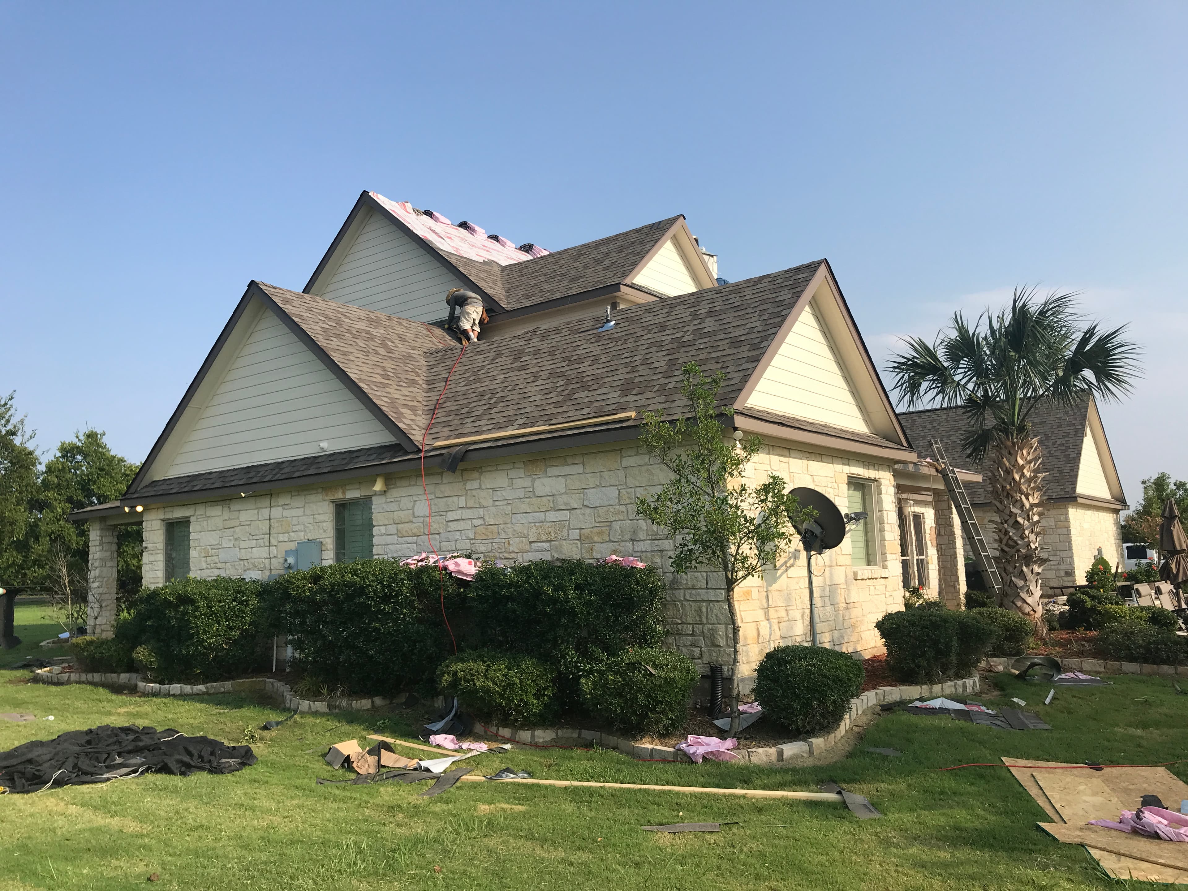 Professional roofing contractor securing asphalt shingles on a pitched stone home roof.