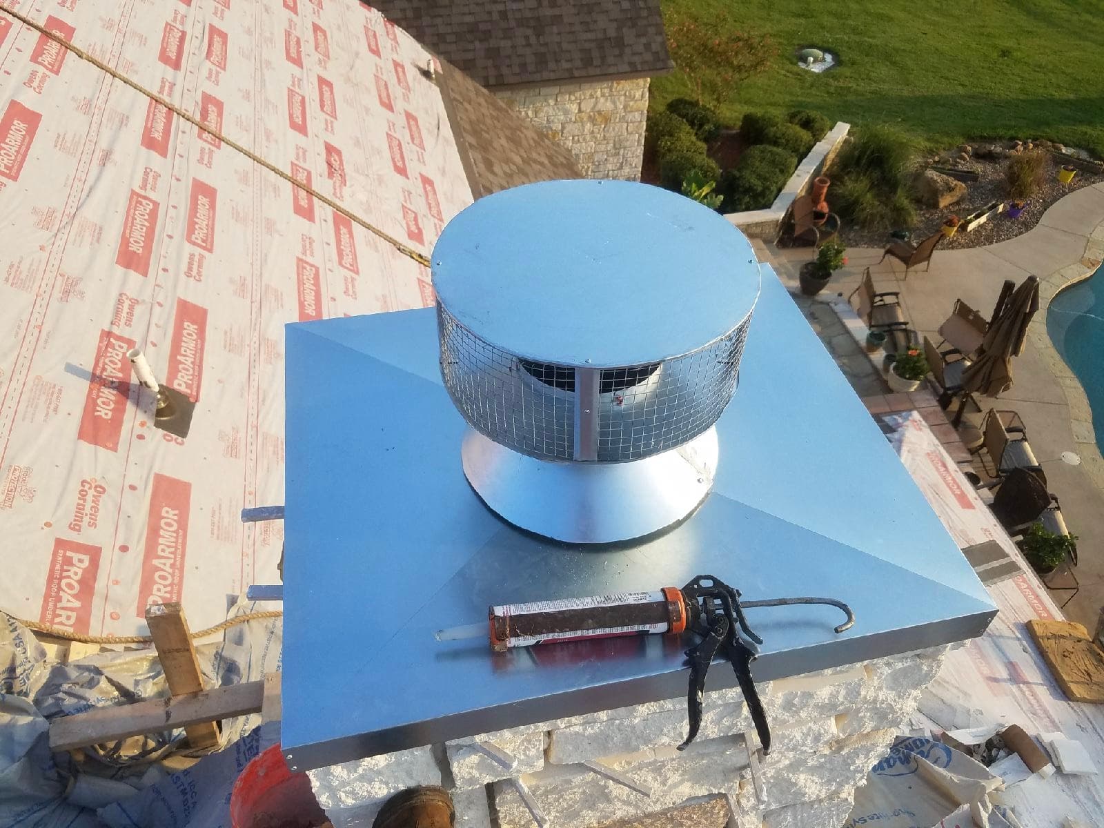 High-angle view of a newly installed custom metal chimney cap with a caulk gun ready for final weatherproofing.