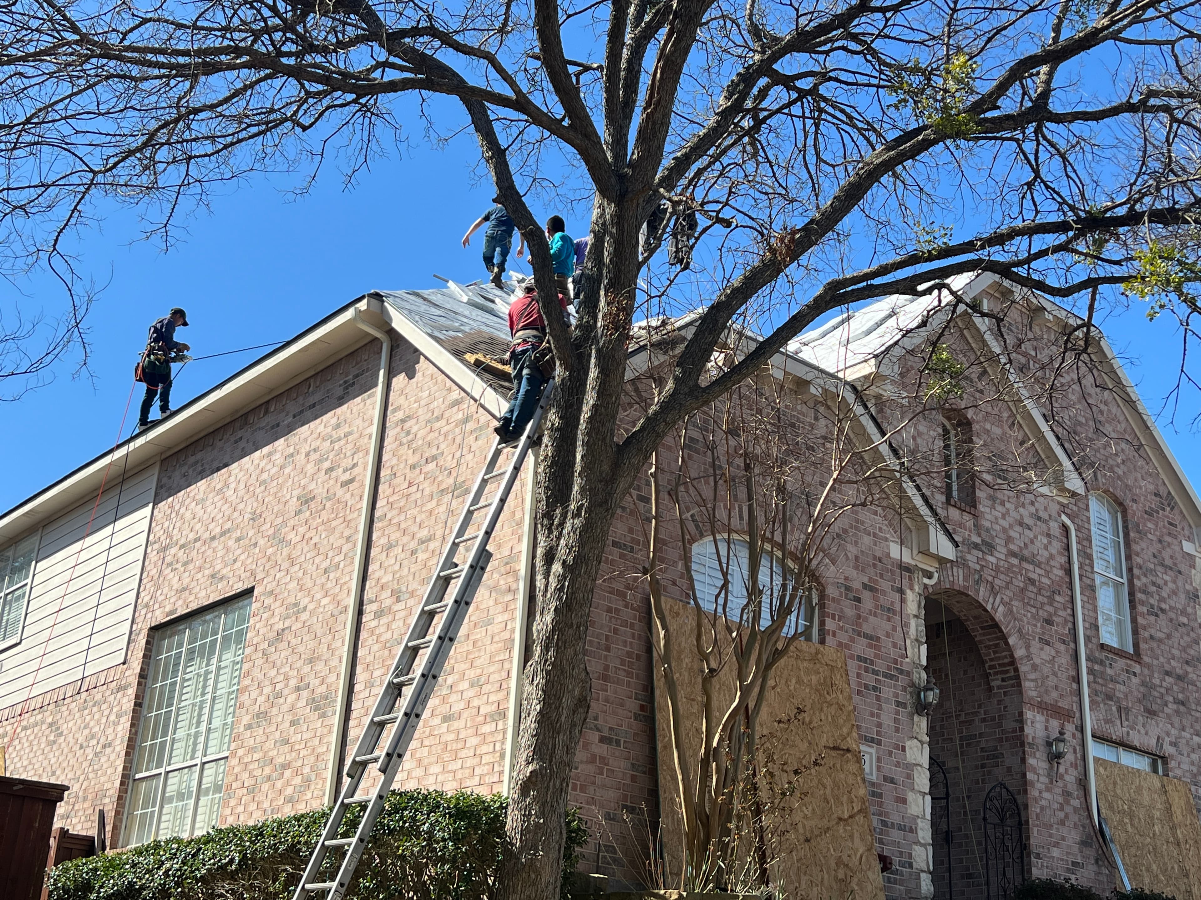 Roofers secured with safety harnesses installing underlayment on a steep-slope brick home roofline.