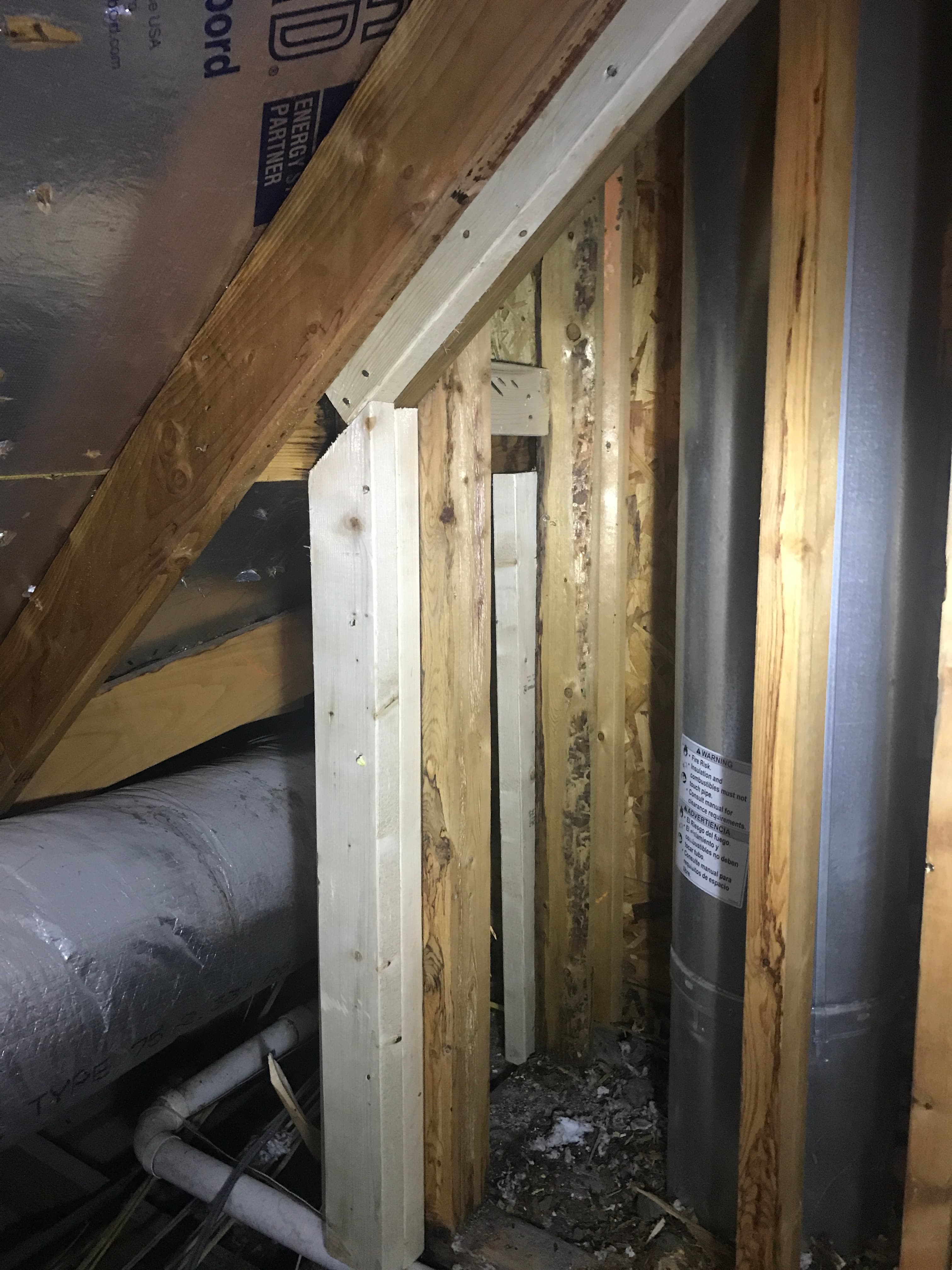 Custom wood framing reinforcement around a double-wall chimney exhaust pipe inside a residential attic space.