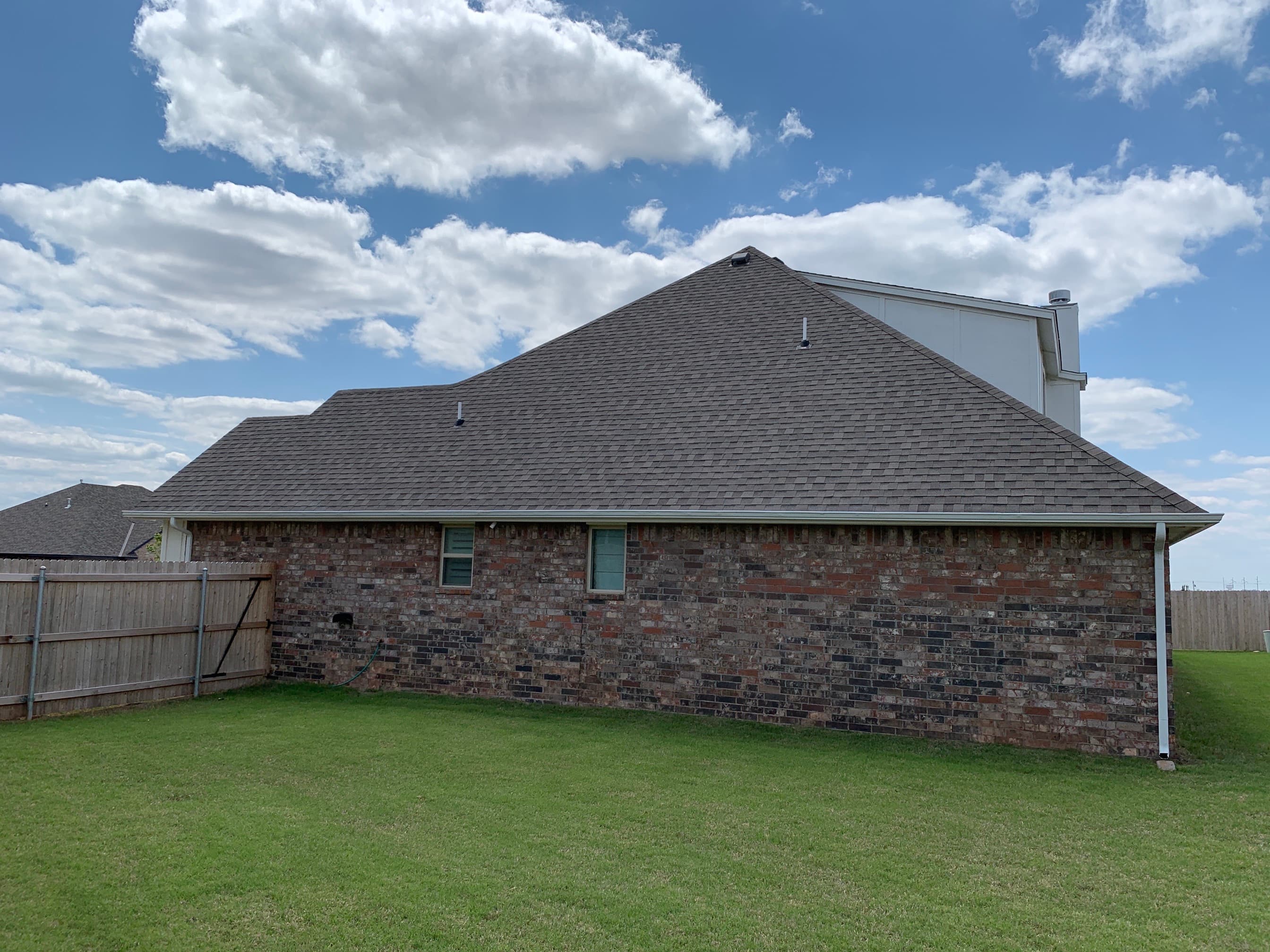Side elevation of an Oklahoma City brick home featuring a newly installed dark architectural shingle roof and white gutters.
