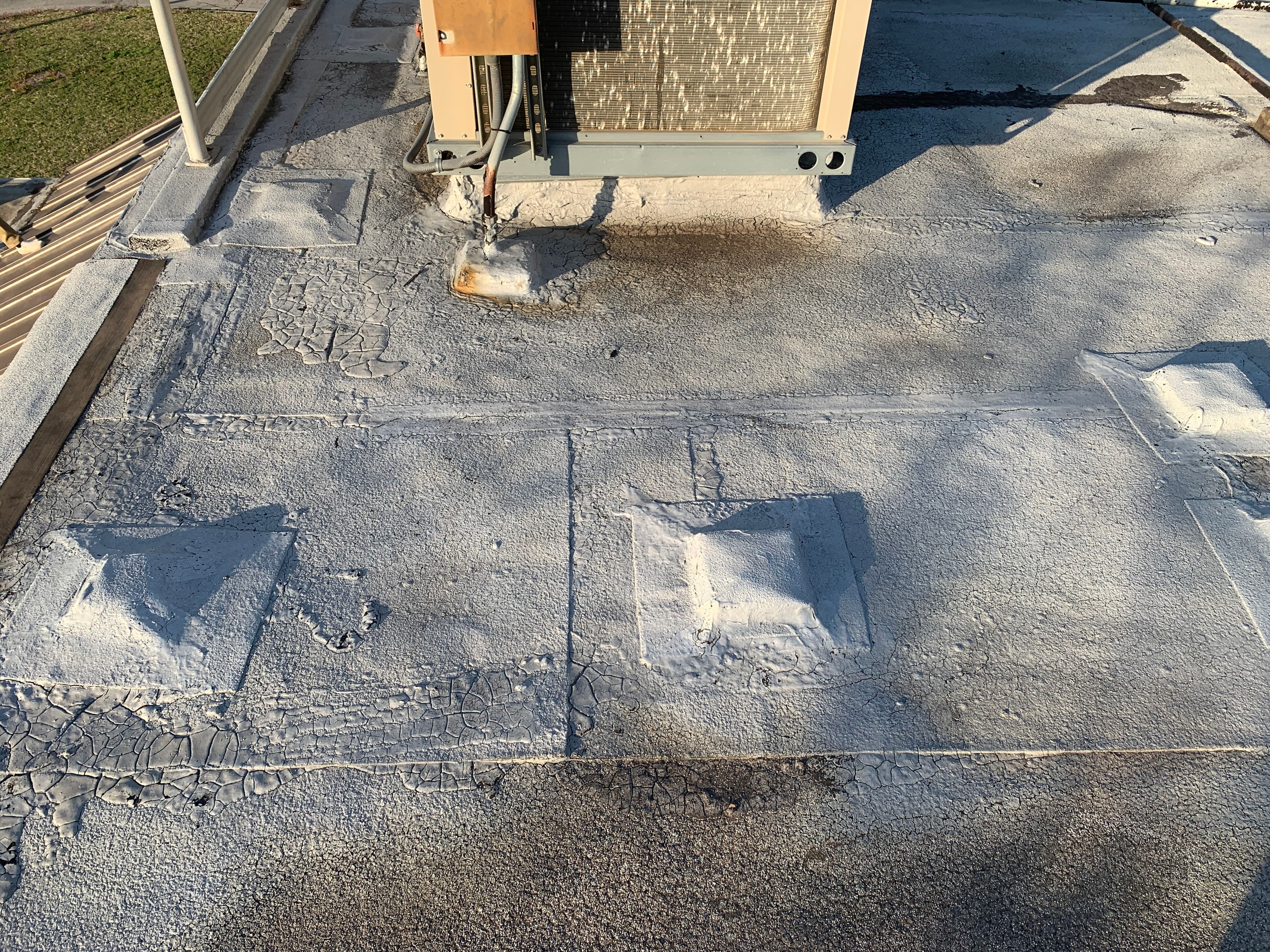 Detailed inspection photo showing cracked elastomeric roof coating and flashed curb supports around a commercial HVAC condenser.