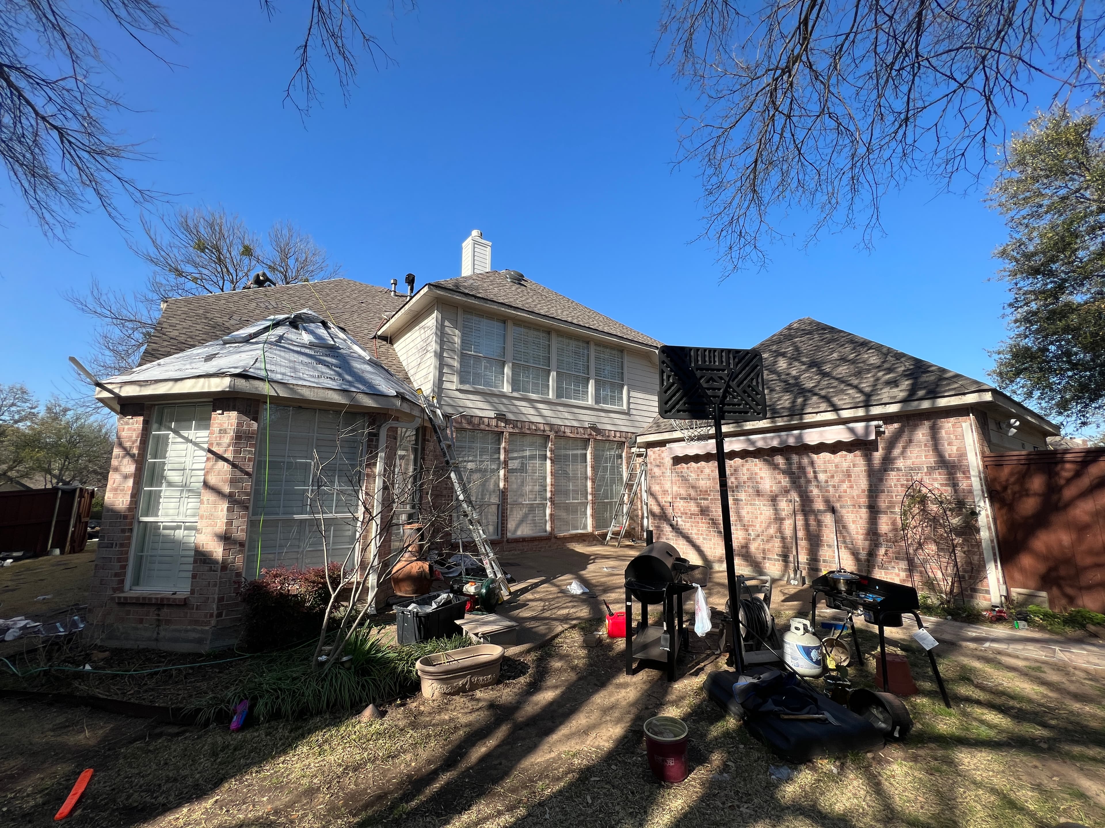 Backyard perspective of a two-story brick home receiving a new roof with synthetic underlayment installed on the turret section.