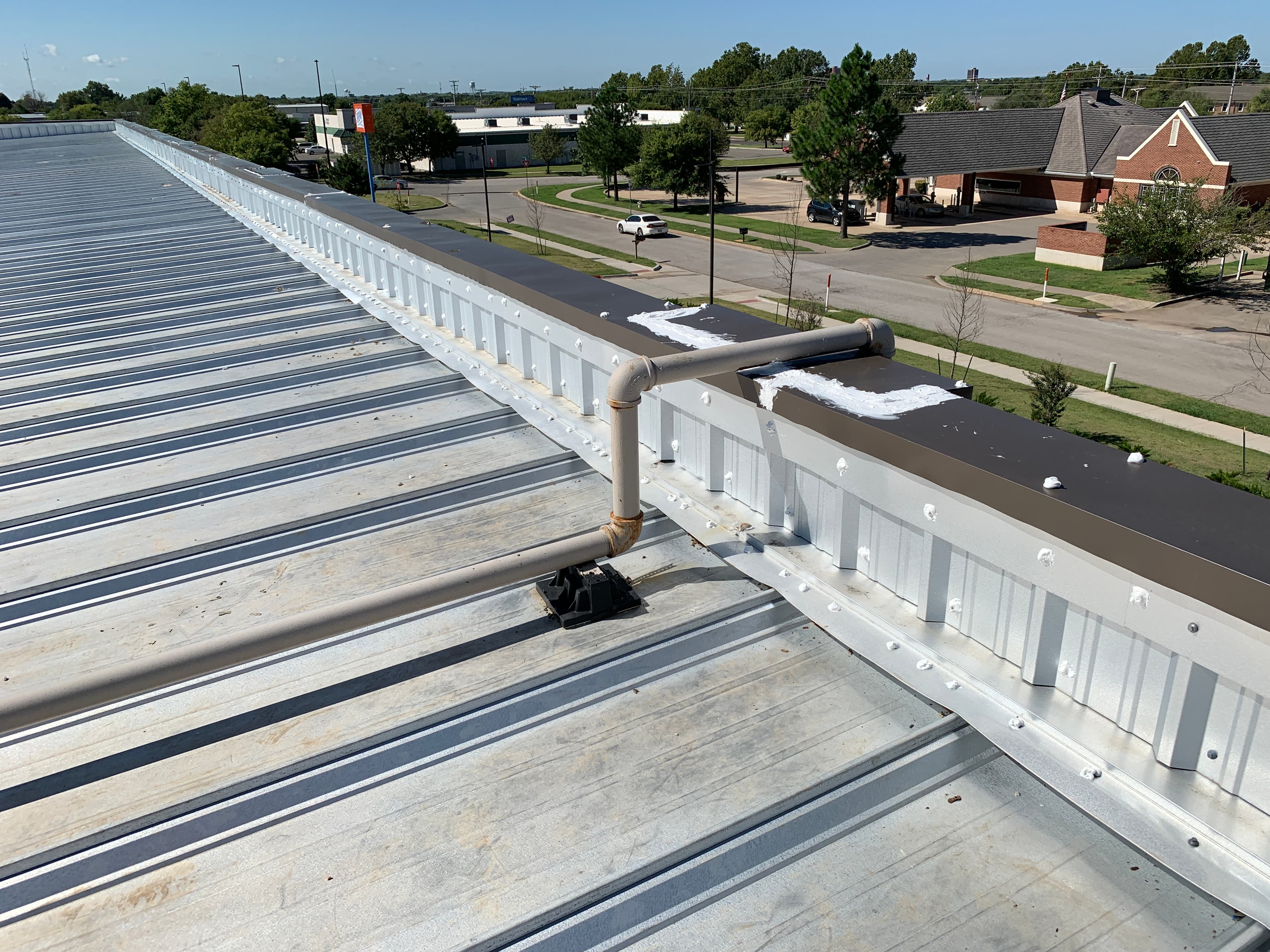 Rooftop utility pipe supported on rubber mounting block crossing over a commercial metal roof parapet wall in Norman, OK.