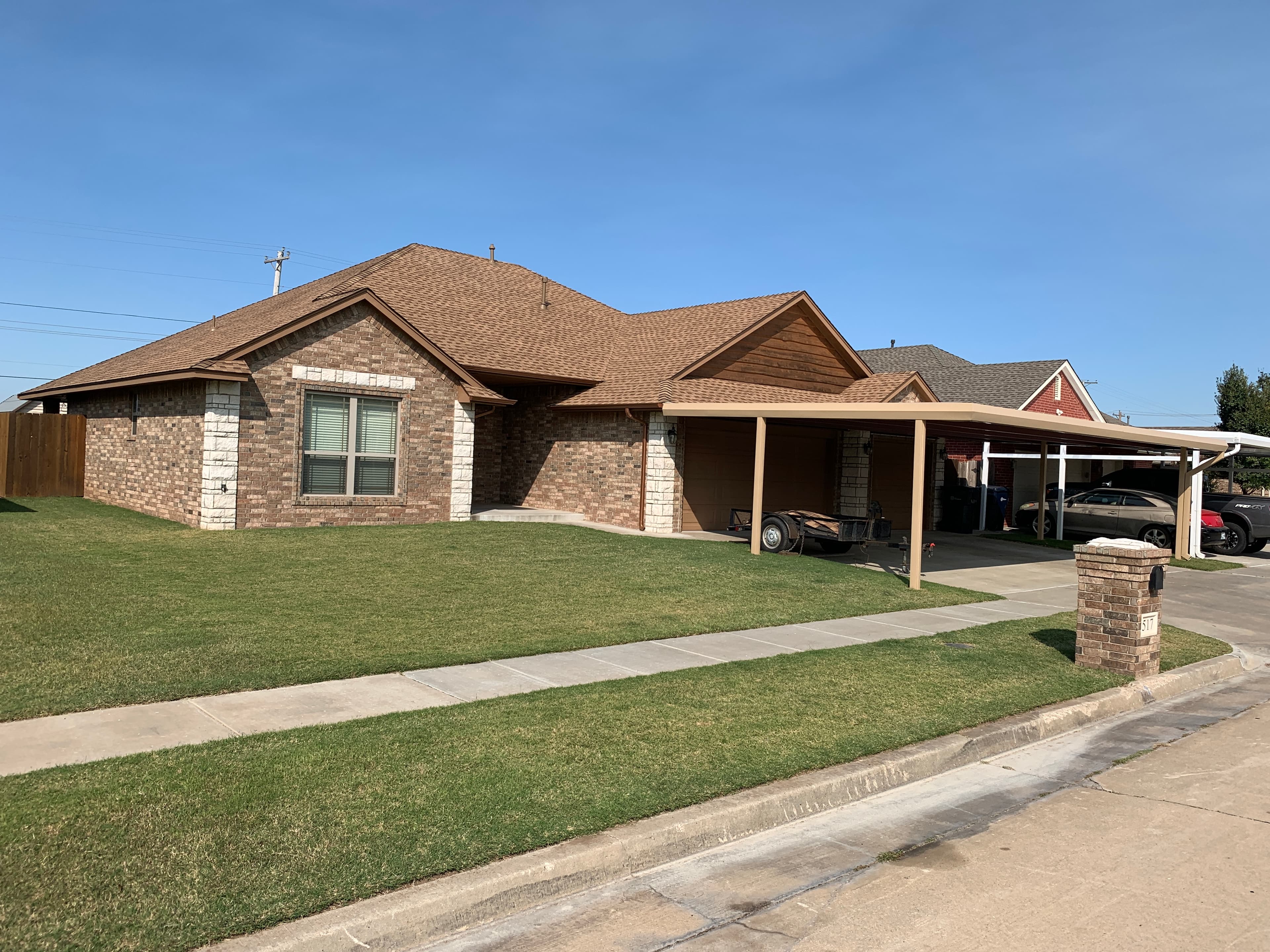 Side angle view of a freshly shingled brick home and carport roof replacement in Oklahoma City, Oklahoma.