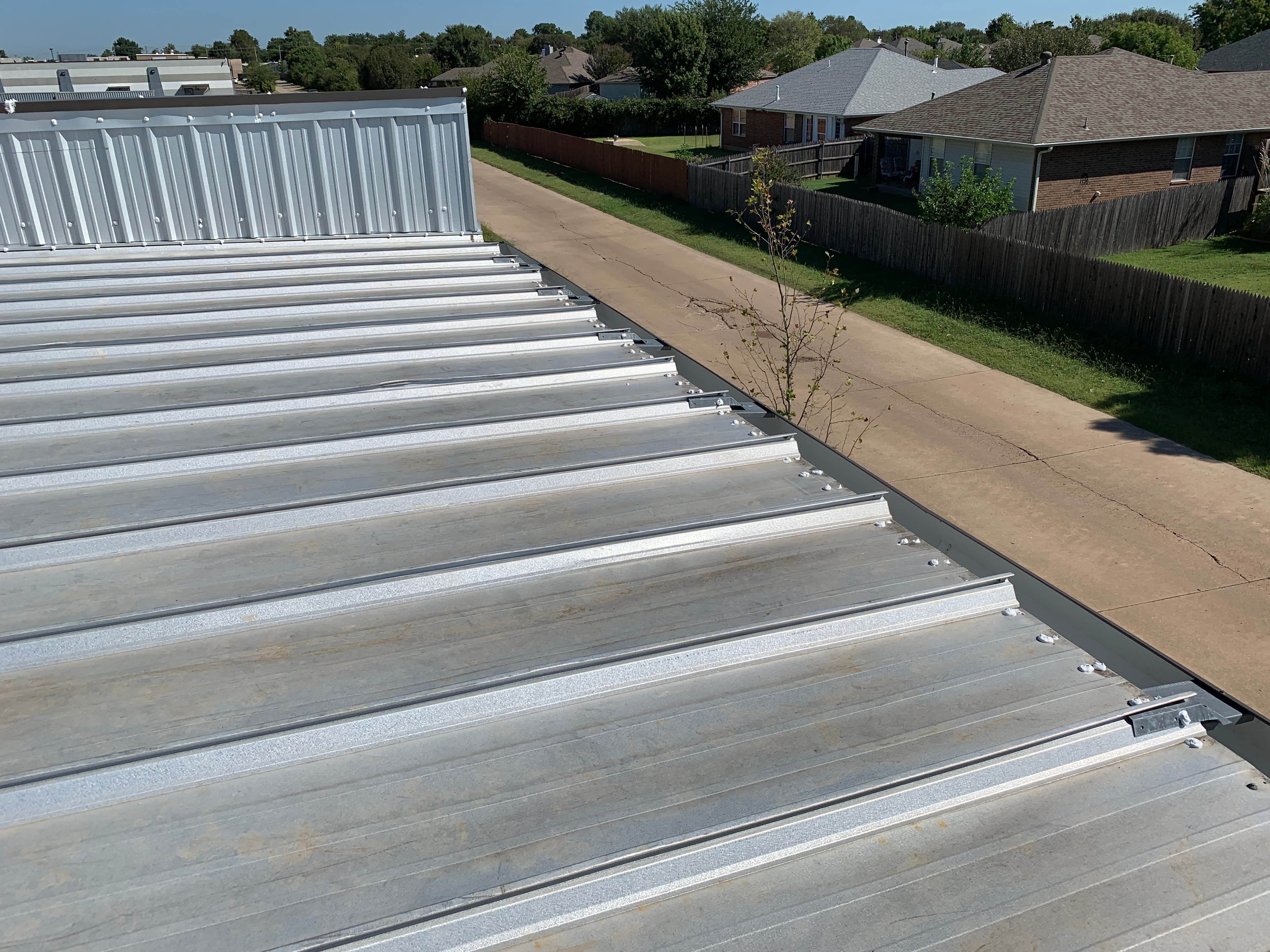 High-angle view of a low-slope commercial metal roof system with custom gutter installation in Norman, OK.