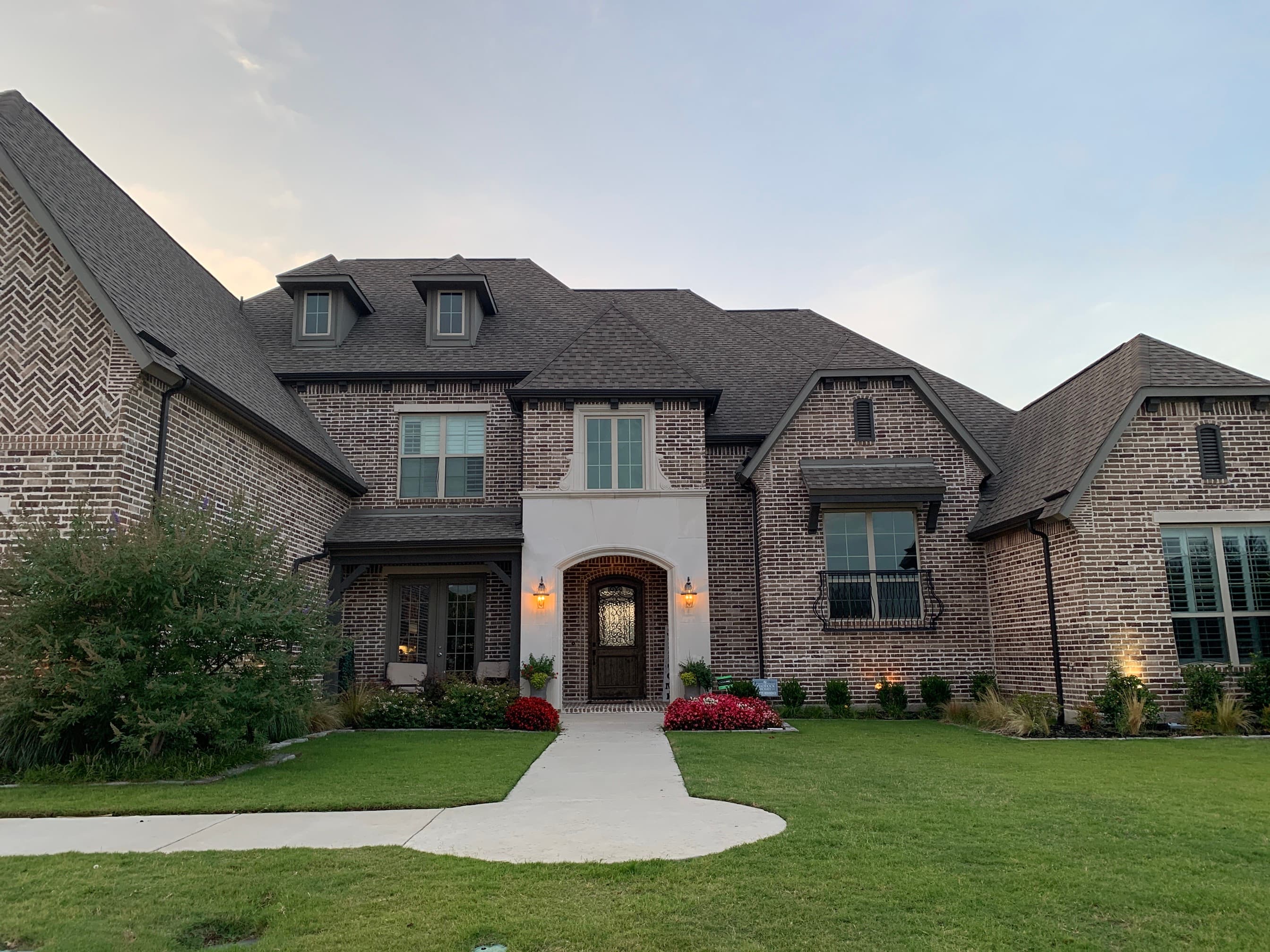 Front view of a luxury multi-gable brick home featuring a newly installed dark architectural asphalt shingle roof and decorative dormers
