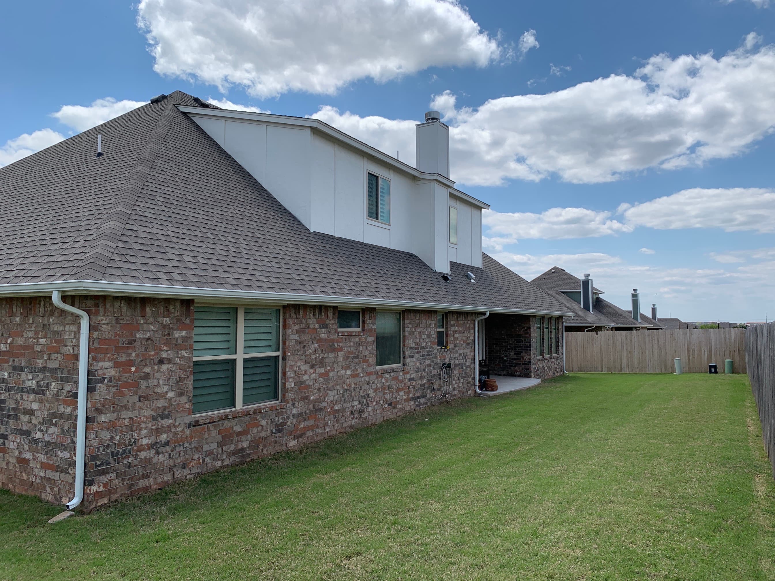 Side angle view of an Oklahoma City house displaying clean roofline edges, new shingles, and seamless white downspouts.