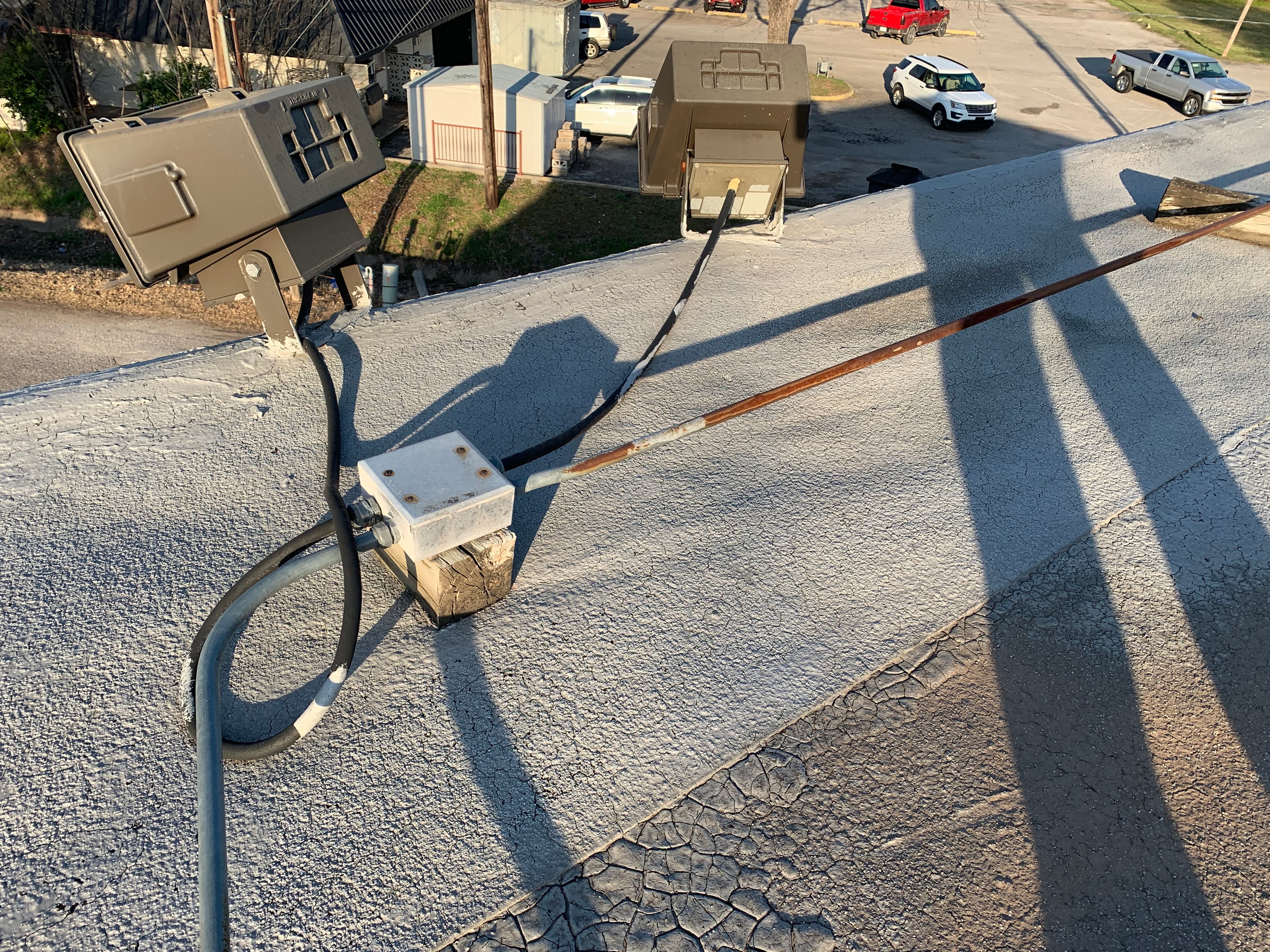 Exterior floodlights and sealed electrical conduit box mounted on a coated commercial flat roof membrane.
