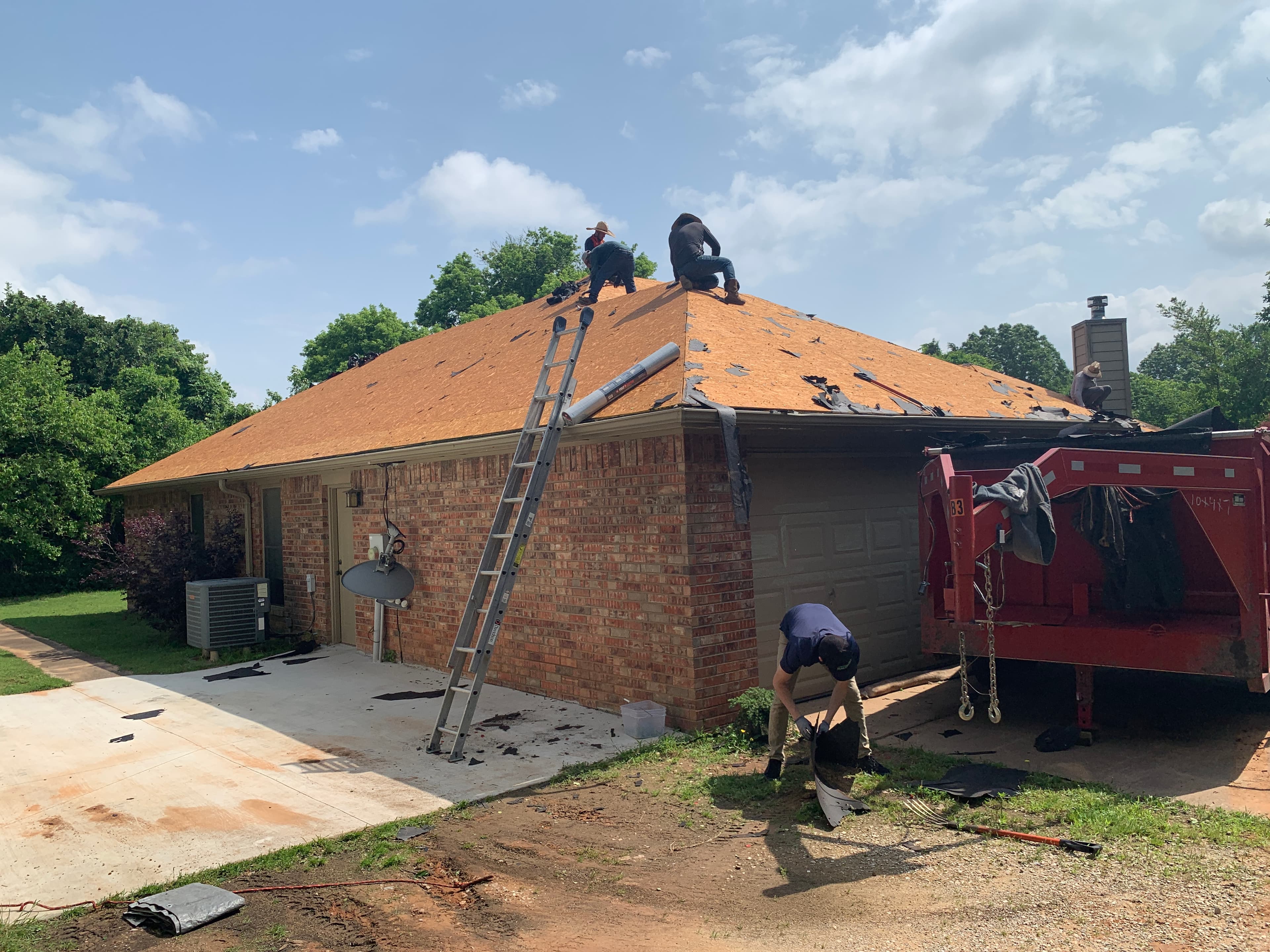 Professional roofing crew removing old shingles down to wood decking on a single-story brick home in Yukon, OK.