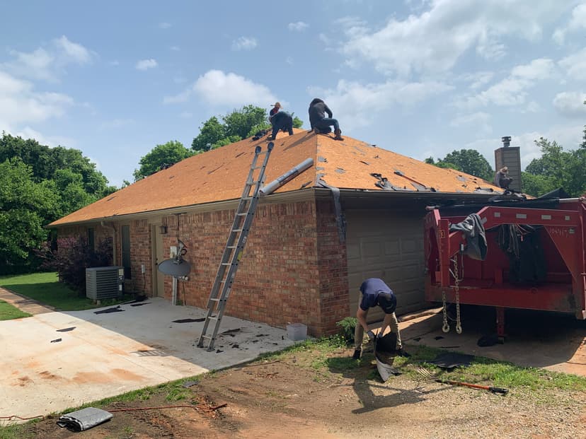 Professional roofing crew removing old shingles down to wood decking on a single-story brick home in Yukon, OK.