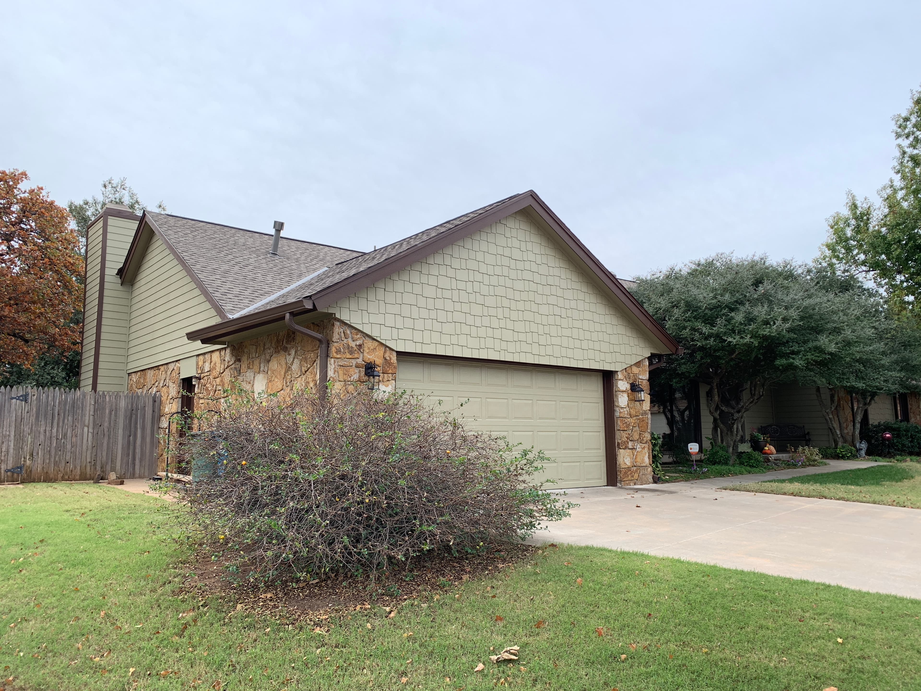 Front garage and driveway view of a stone-accent home in Edmond, OK featuring a newly installed brown architectural asphalt shingle roof.