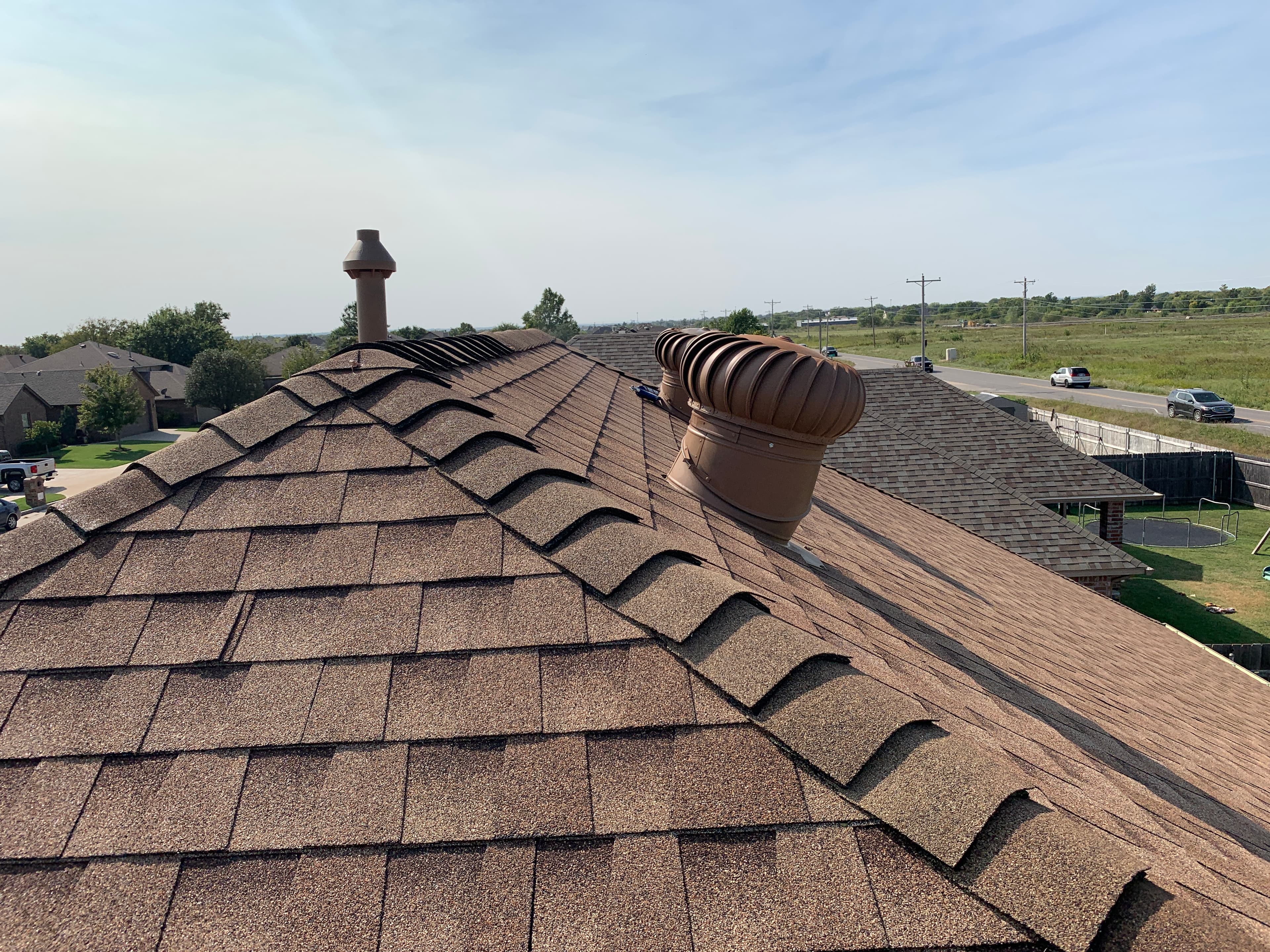 Newly installed brown architectural shingle roof featuring attic turbine vents and ridge cap shingles in Oklahoma City, OK.
