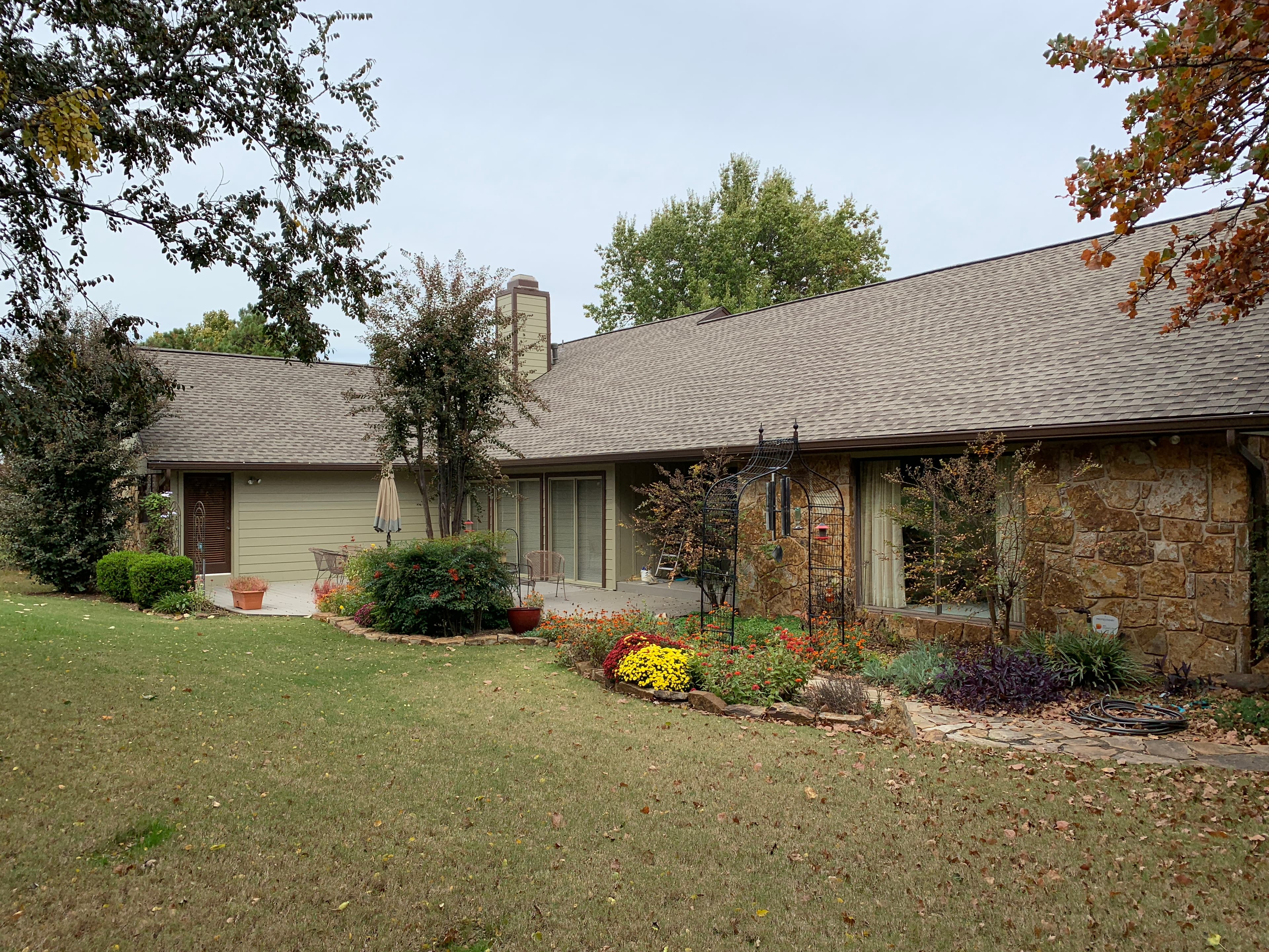 Full backyard elevation of an Edmond home featuring a large multi-slope architectural shingle roof, siding chimney box, and patio garden.