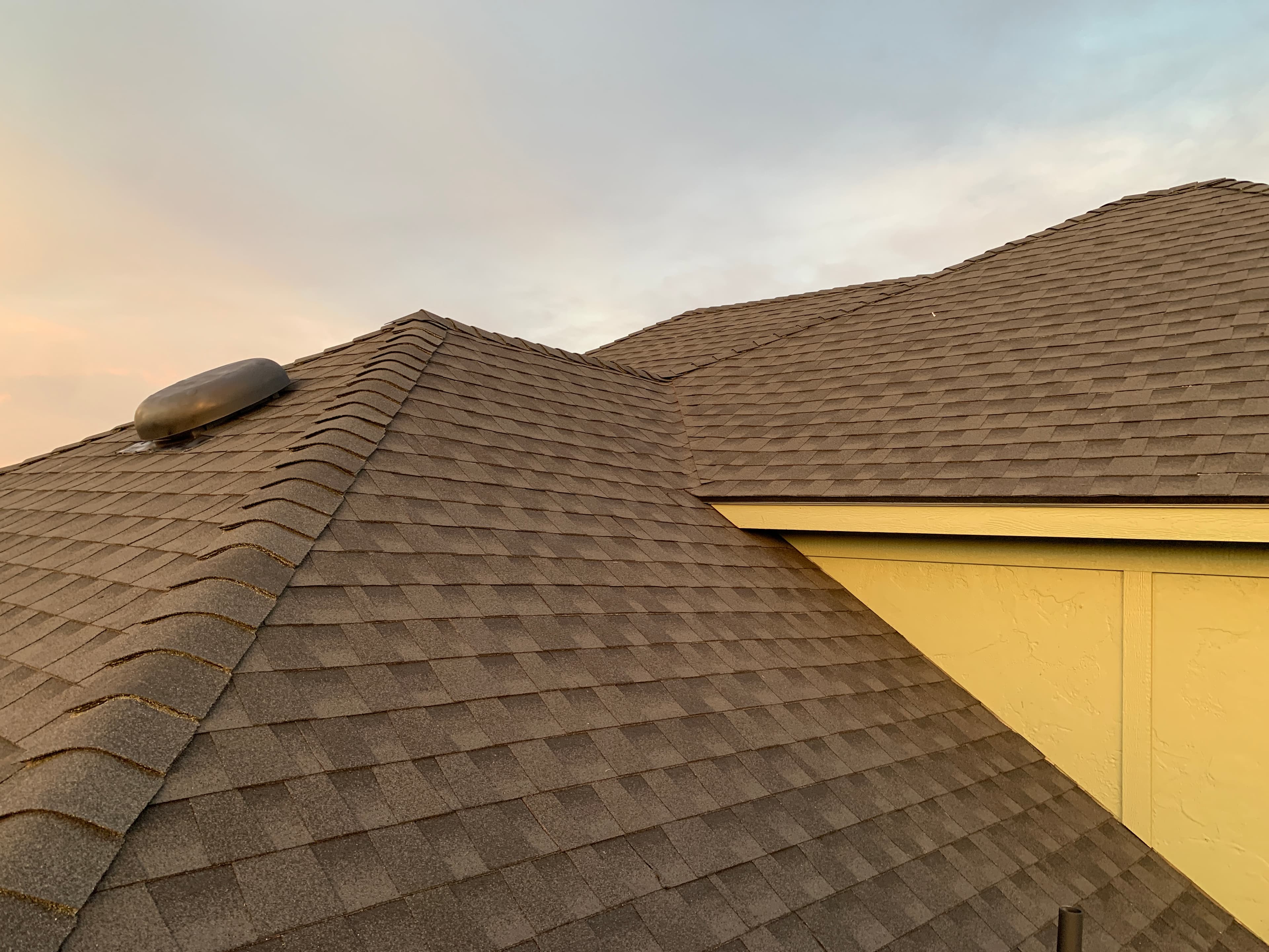 Rooftop view of newly installed dark architectural shingles, hip ridge caps, and low-profile attic vent in Norman, OK.