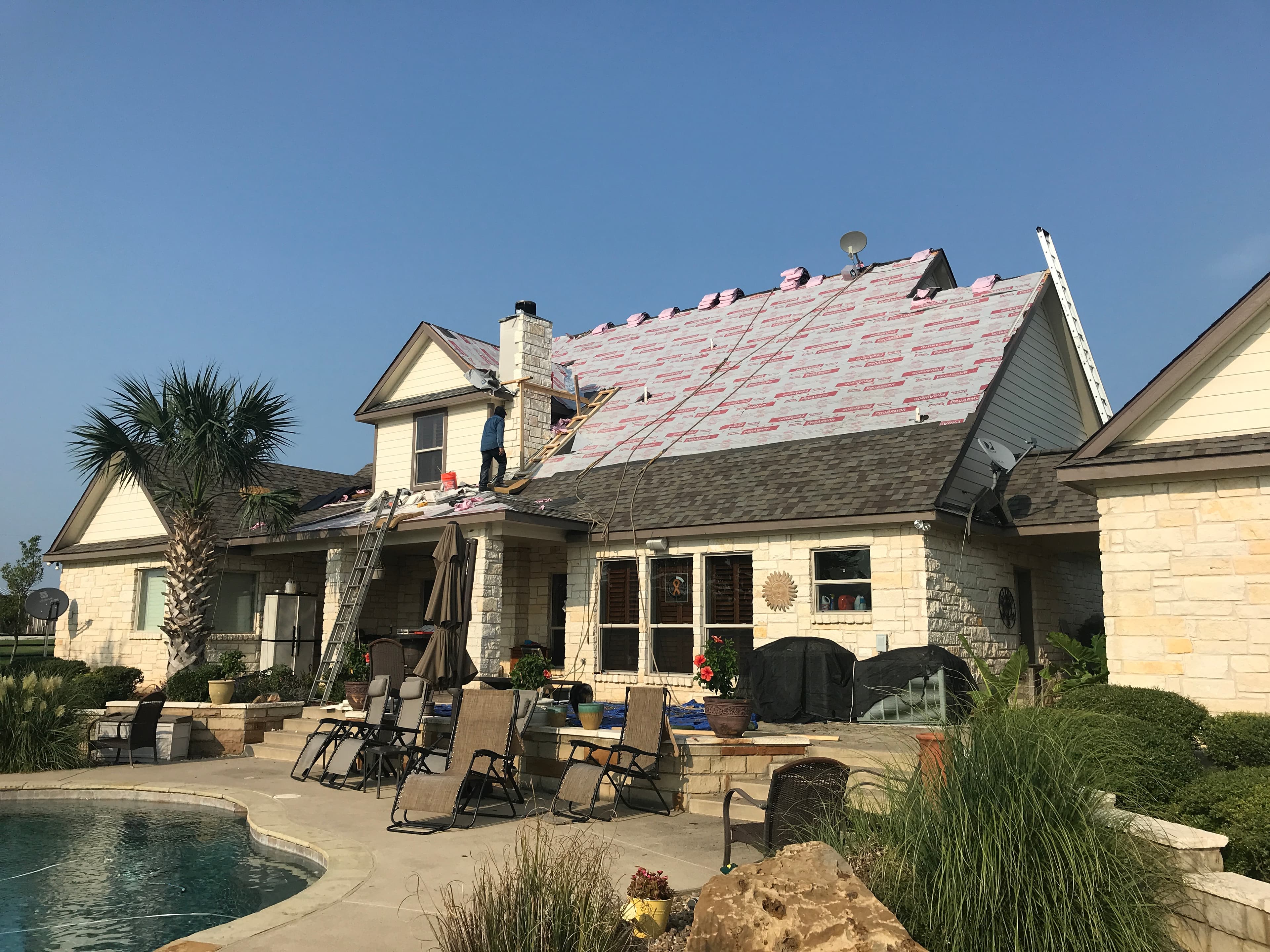 Overview of a poolside stone house undergoing full roof replacement with synthetic underlayment applied.