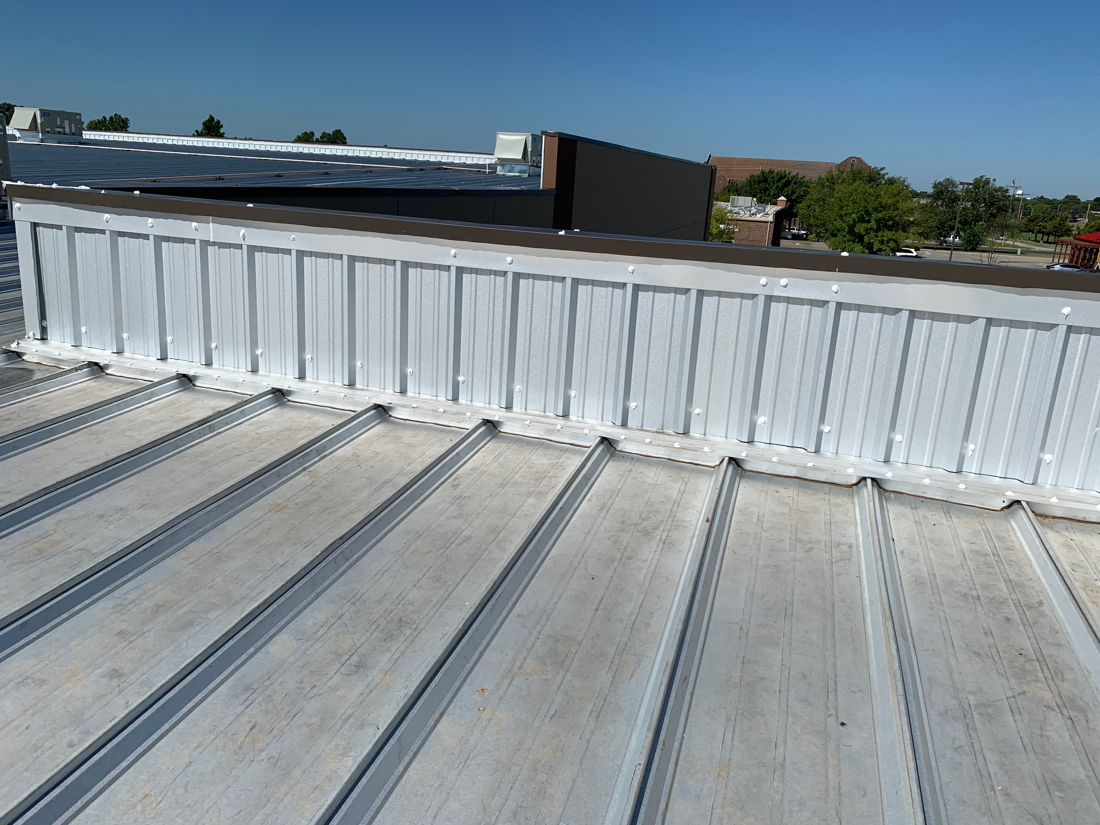 Corrugated metal parapet wall panels and dark perimeter coping cap on a commercial metal roof in Norman, OK.