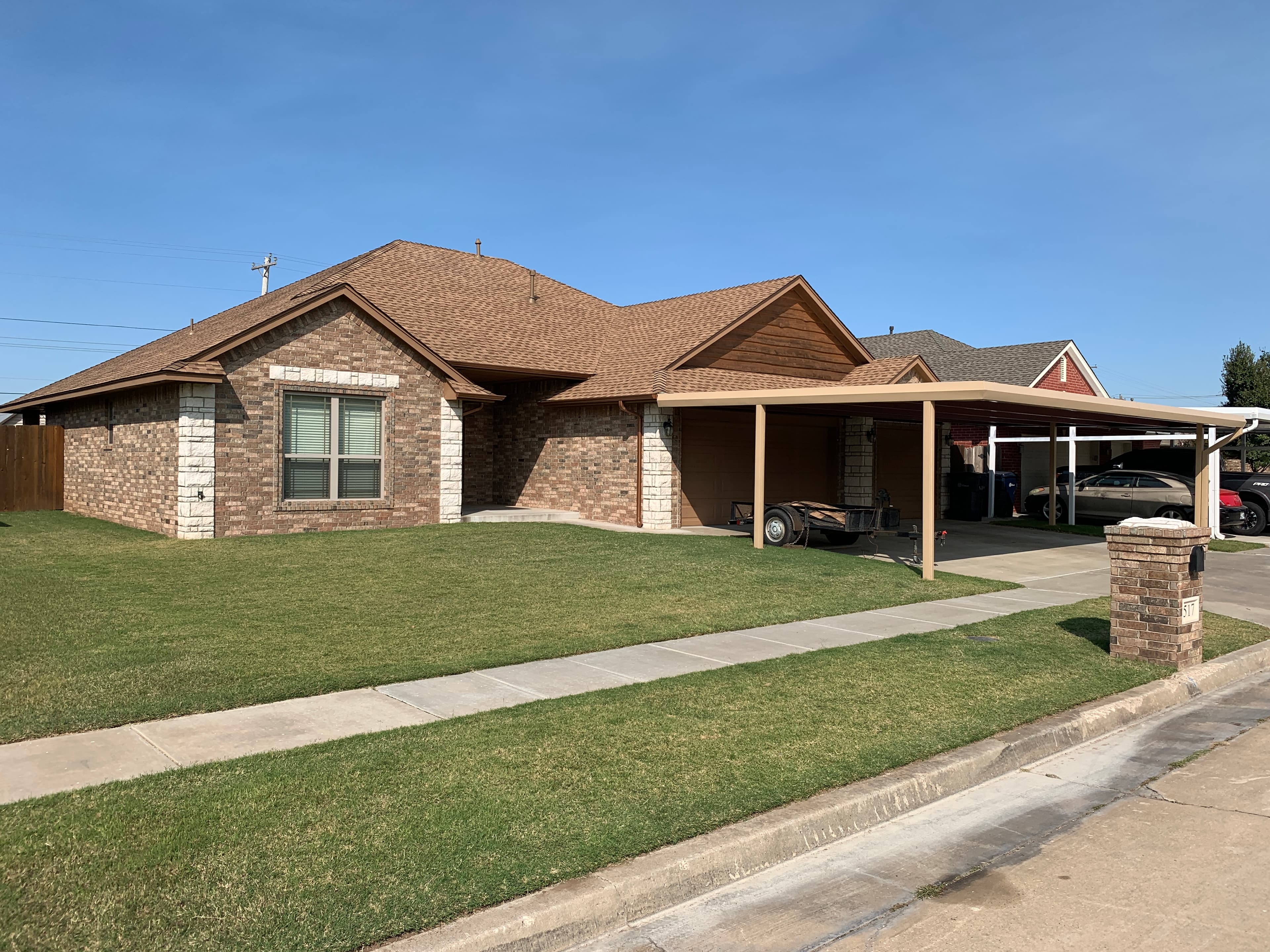 Completed brown asphalt shingle roof replacement on a brick ranch home with an attached carport in Oklahoma City.