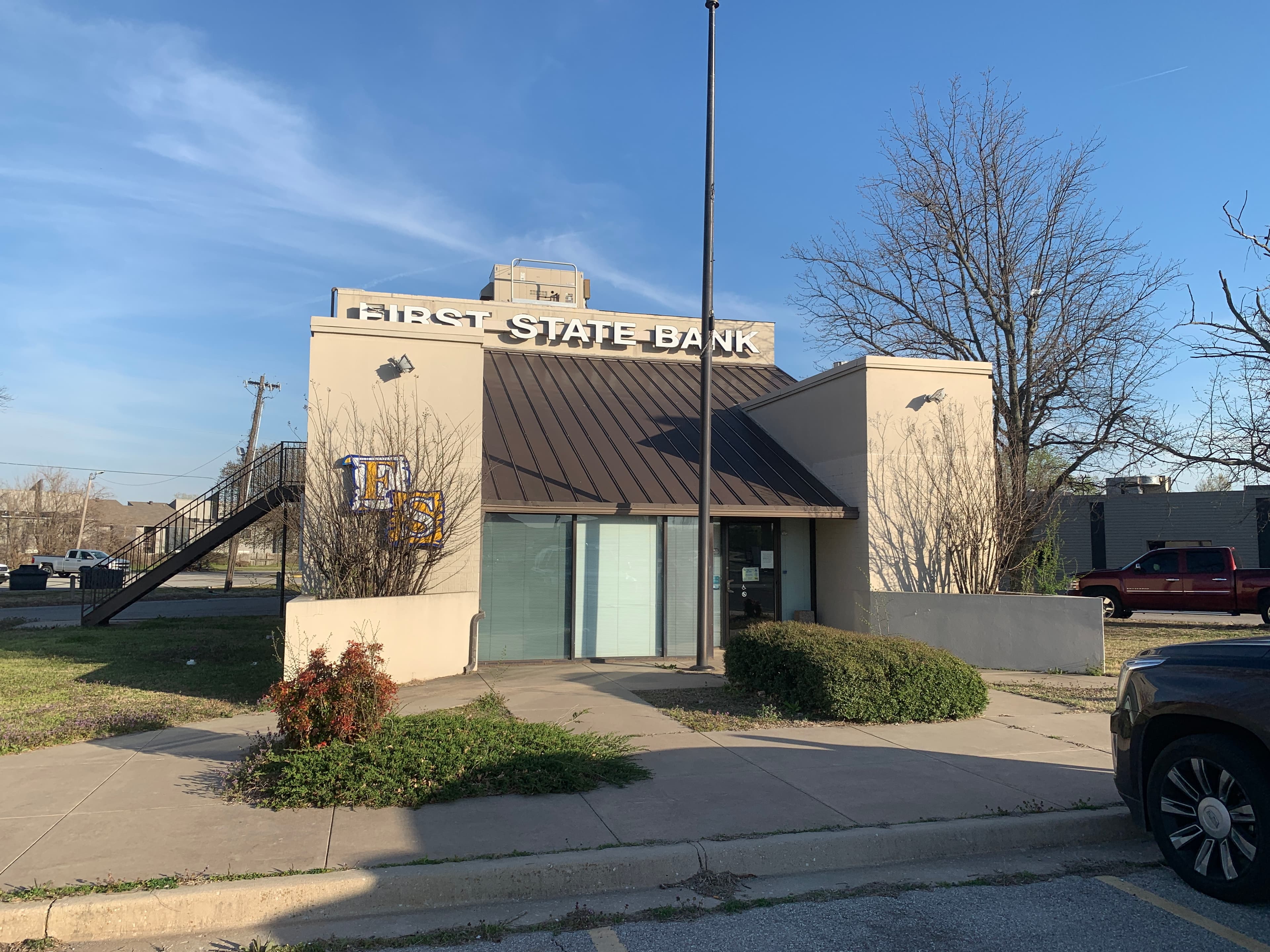 Exterior front view of First State Bank showing a bronze standing seam metal entrance roof and stucco commercial building facade.